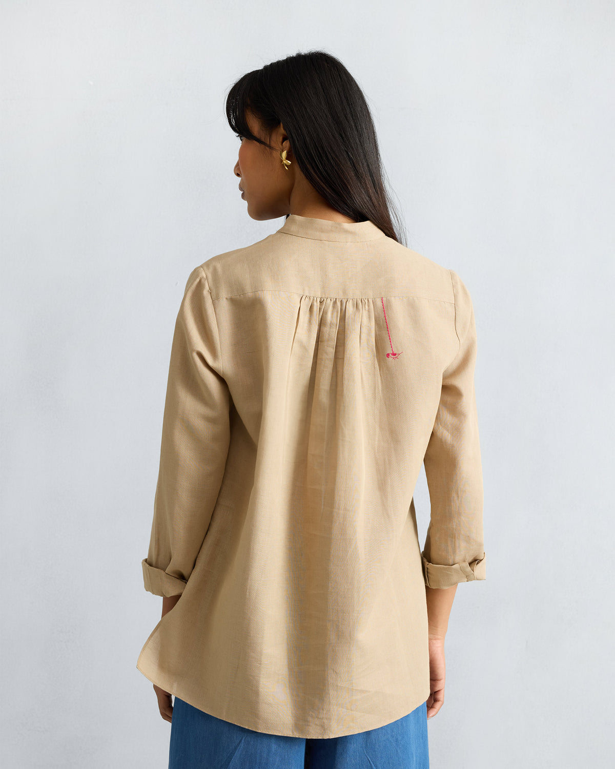 Back of a beige mandarin collar top with a pink embroidered bird.