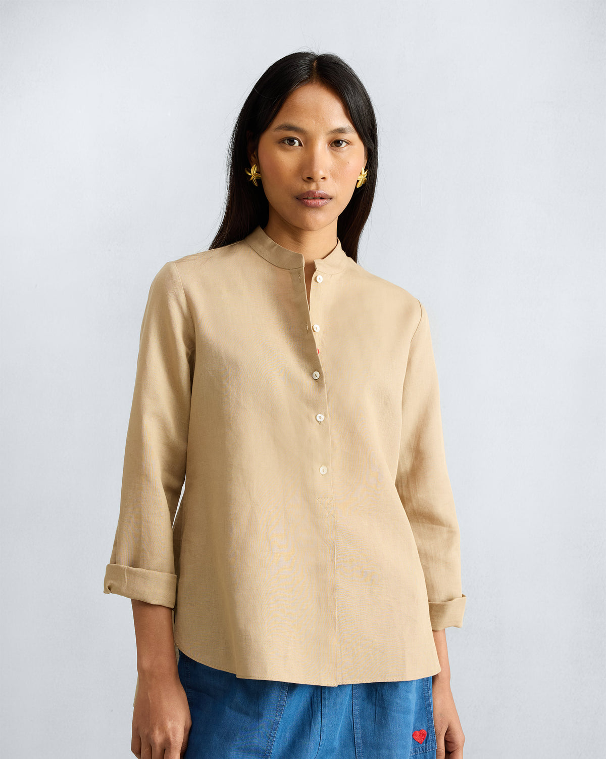 Person wearing a beige mandarin collar top with a button placket.