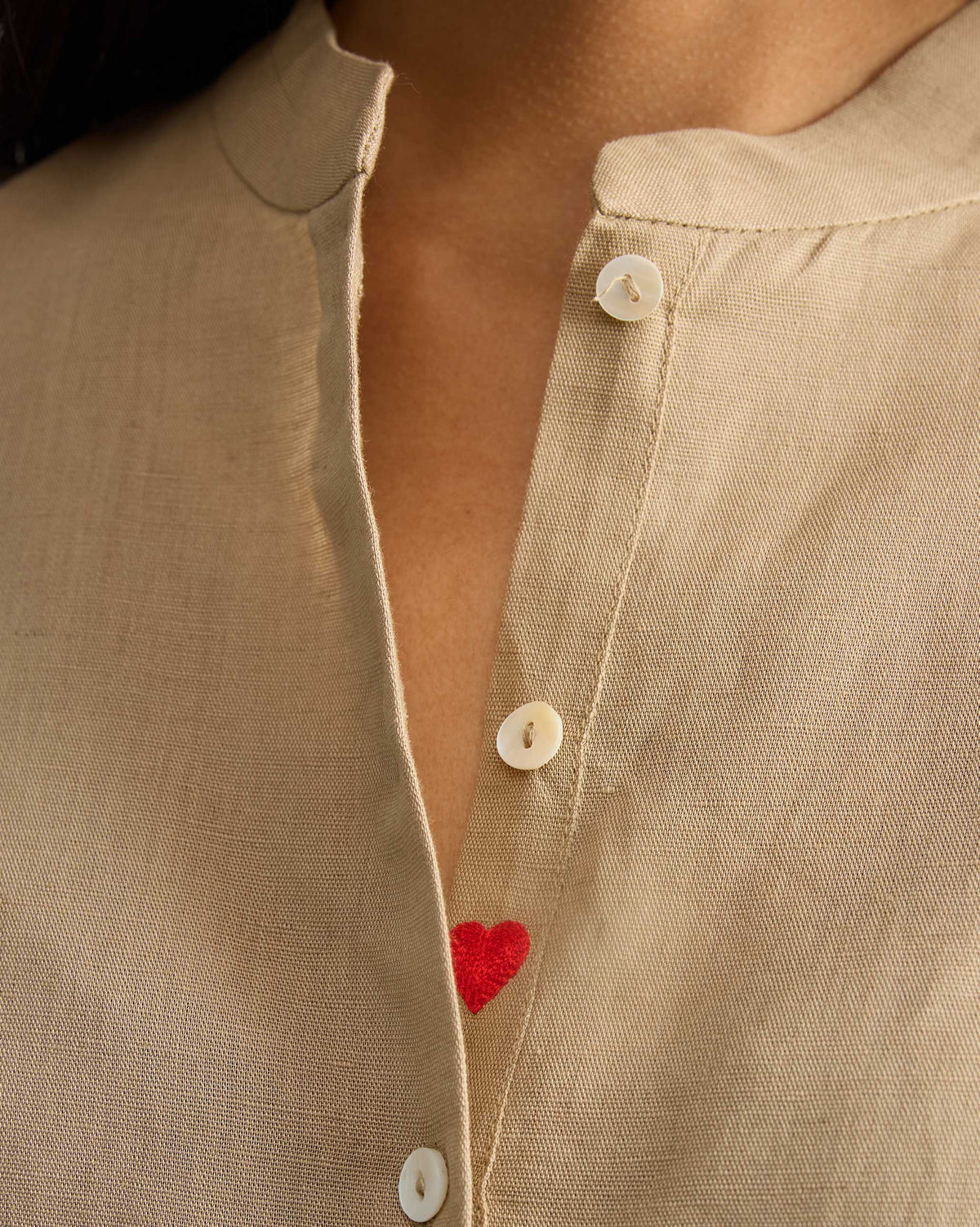 Close-up of the beige mandarin collar and a red embroidered heart on the placket.
