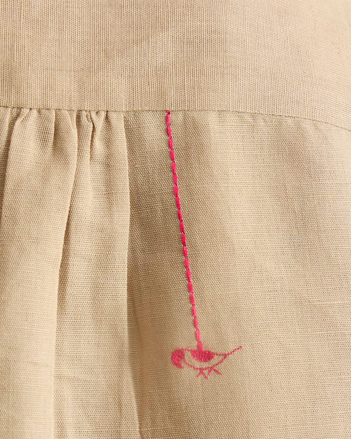 Close-up of a pink embroidered bird on the beige mandarin collar top.