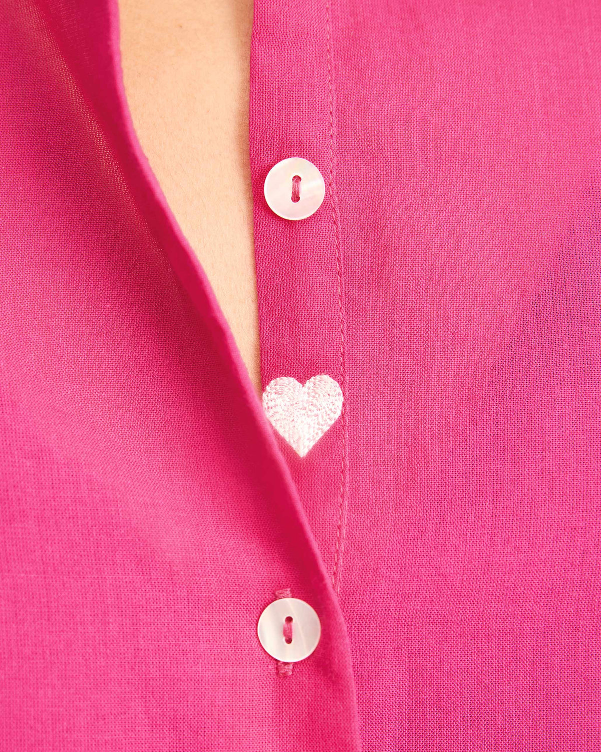 Close-up of a white heart on a fuchsia mandarin collar top.