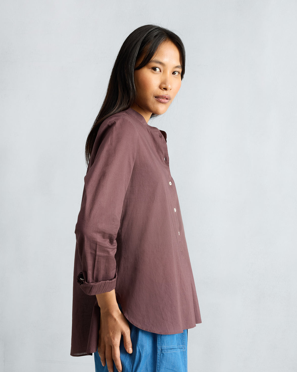 Side view of a chocolate plum mandarin collar top with a curved hem.
