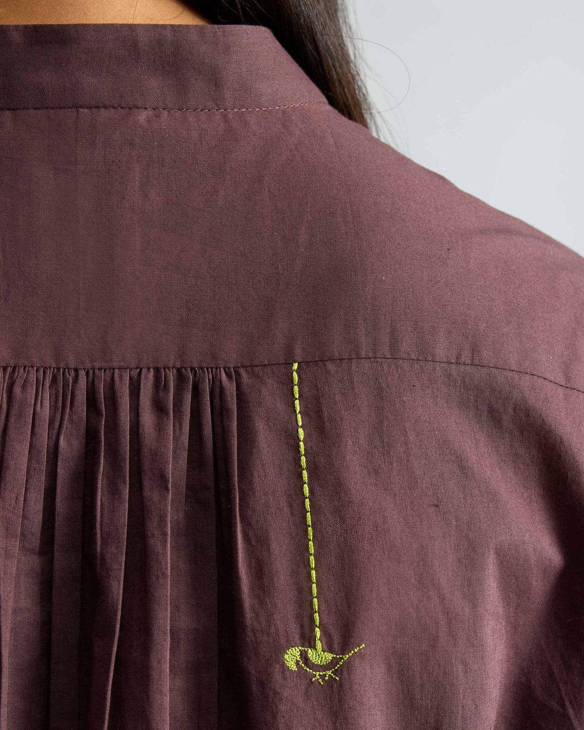 Close-up of a green parrot on a chocolate plum mandarin collar top.