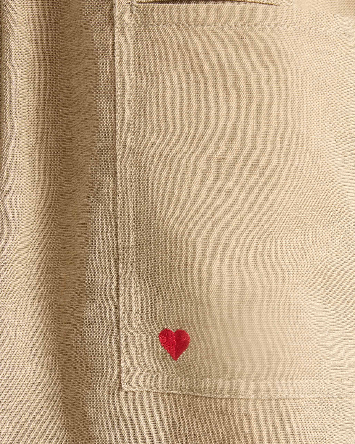 Close-up of beige Yoka Trousers pocket with a small red heart embroidered on it.