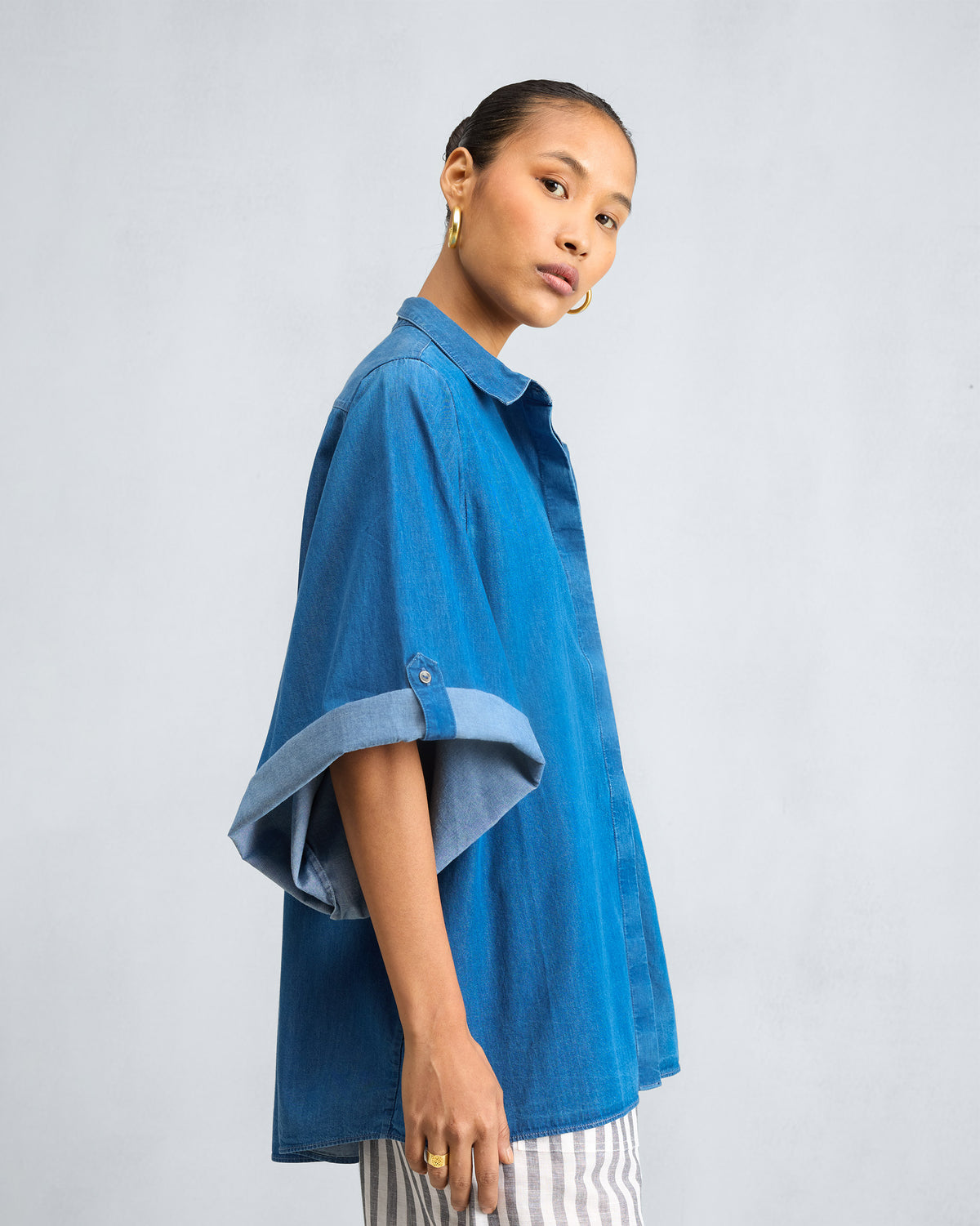 Side view of a blue denim drop armhole shirt with rolled cuffs.