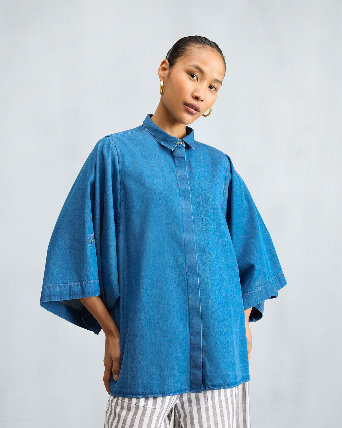 Person wearing a blue denim drop armhole shirt.