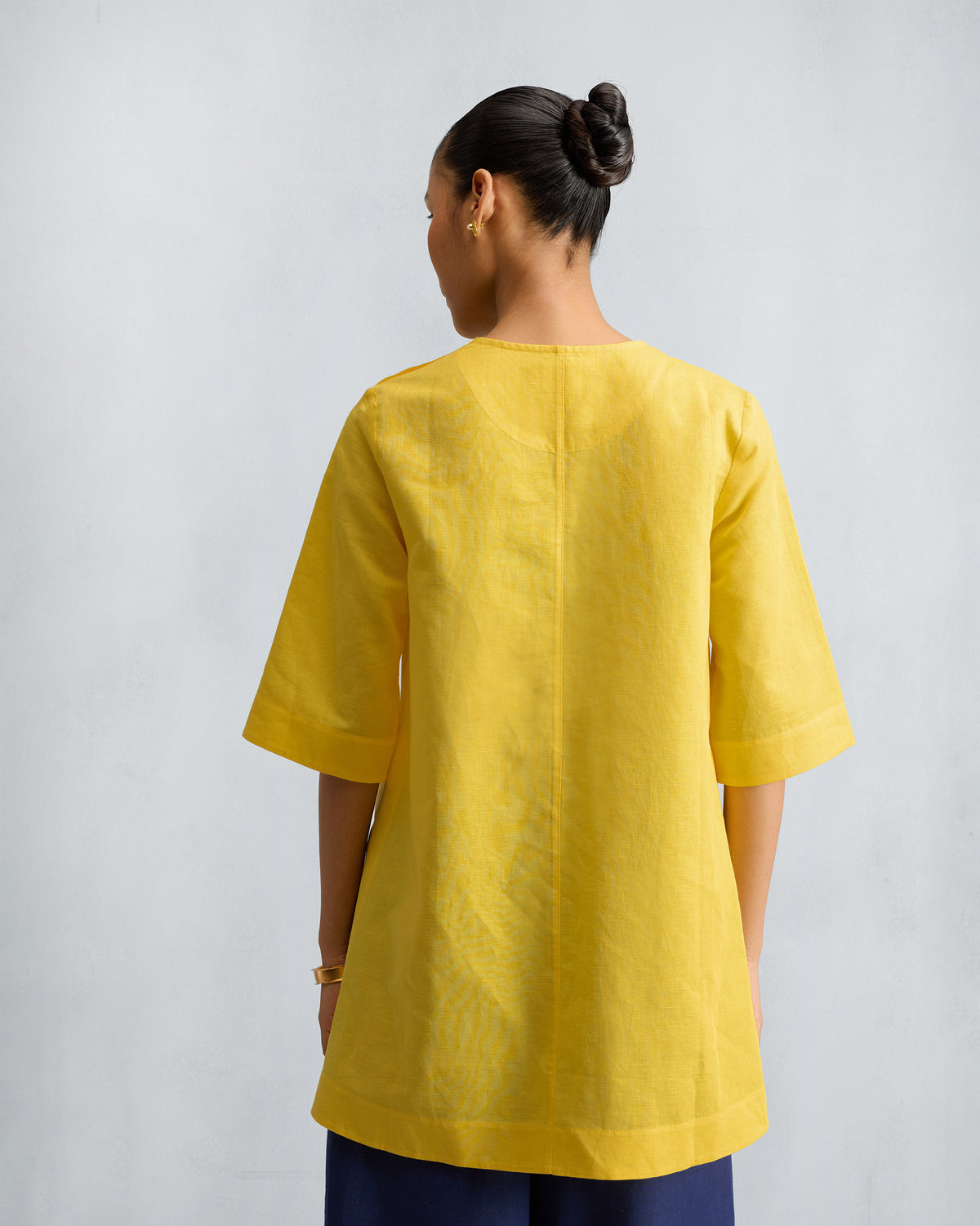 Back of a yellow High Slit Top with a center seam and wide sleeves.
