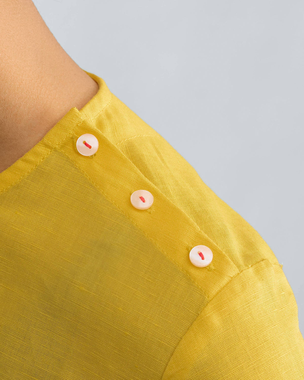 Close-up of red-stitched buttons on the shoulder of a yellow High Slit Top.