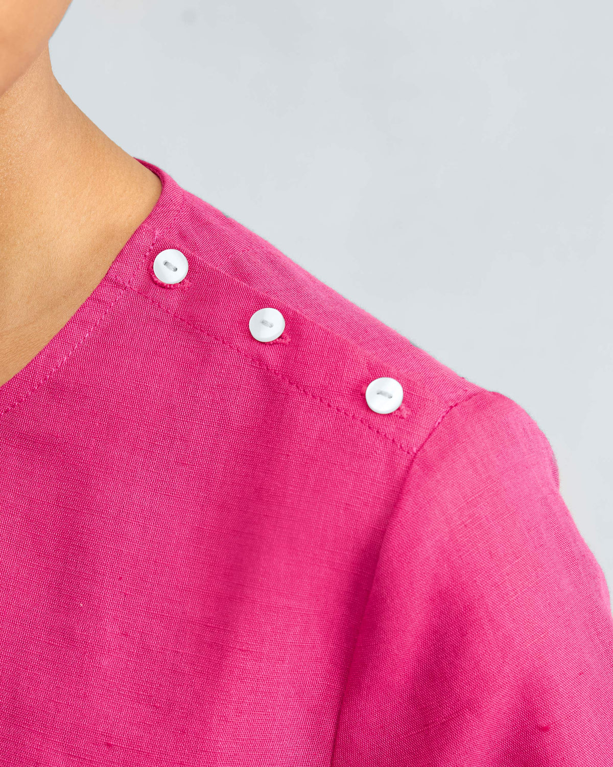 Close-up of a fuchsia top with white shoulder buttons.