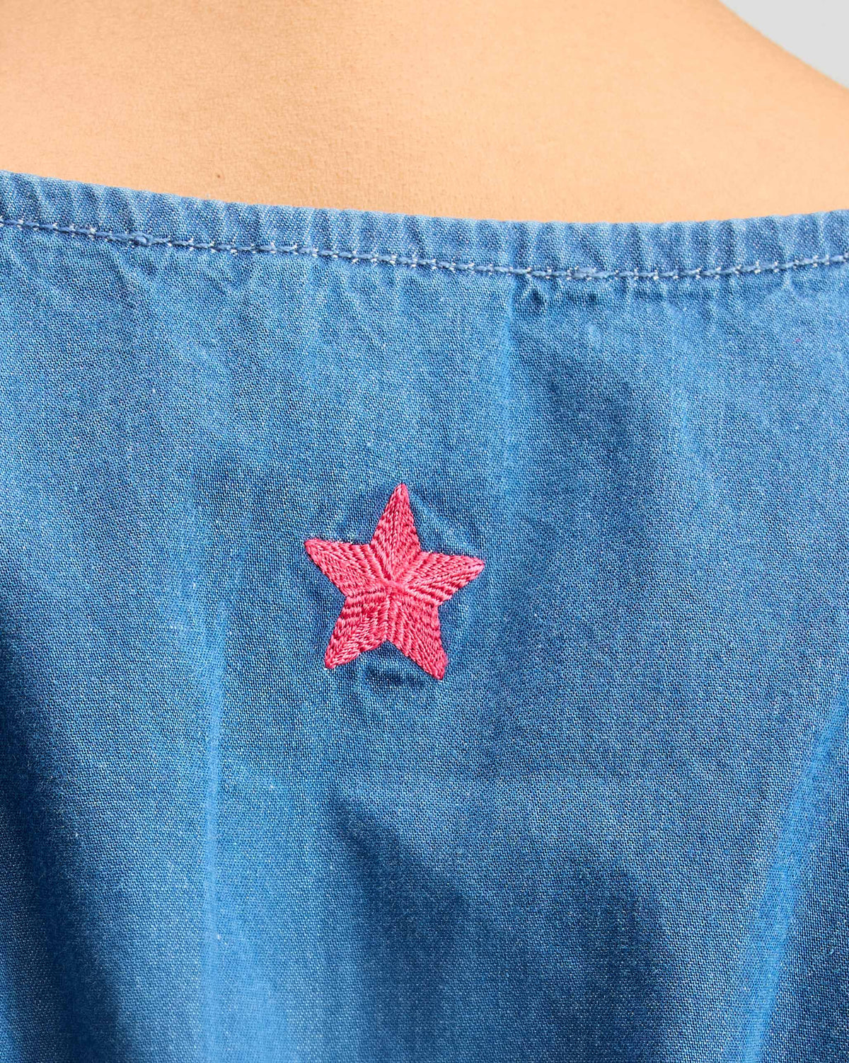 Close-up of a denim short racerback dress with a pink star on the back.