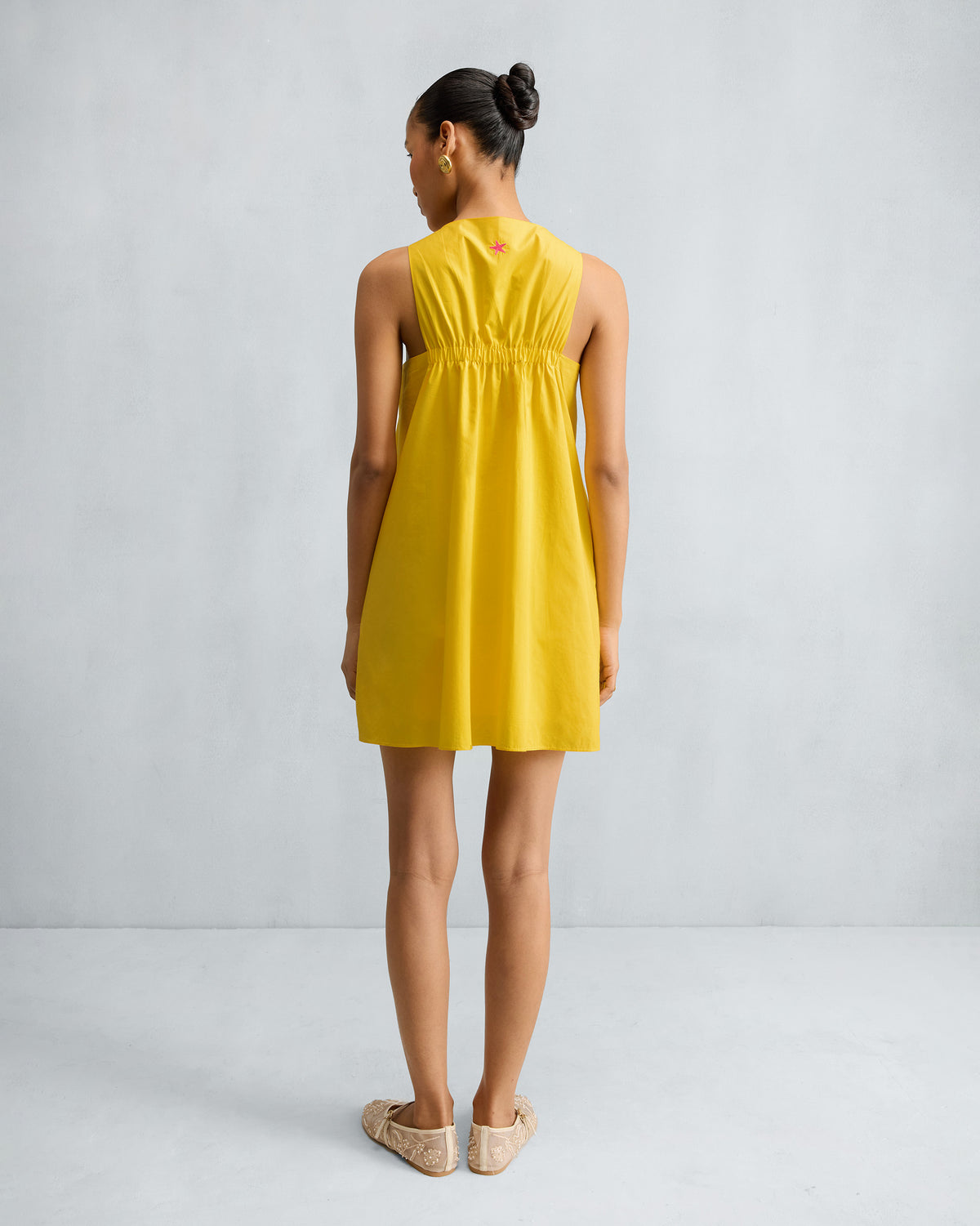 Back of a yellow short racerback dress with a gathered panel.
