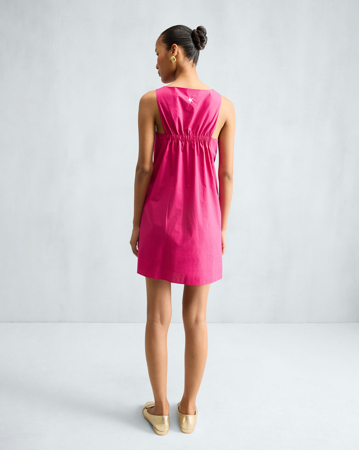 Back of a fuchsia short racerback dress with elastic gathering and a white star.