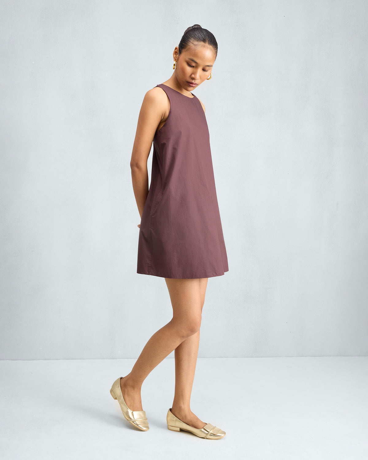 Person wearing a chocolate plum short racerback dress at a slight angle.