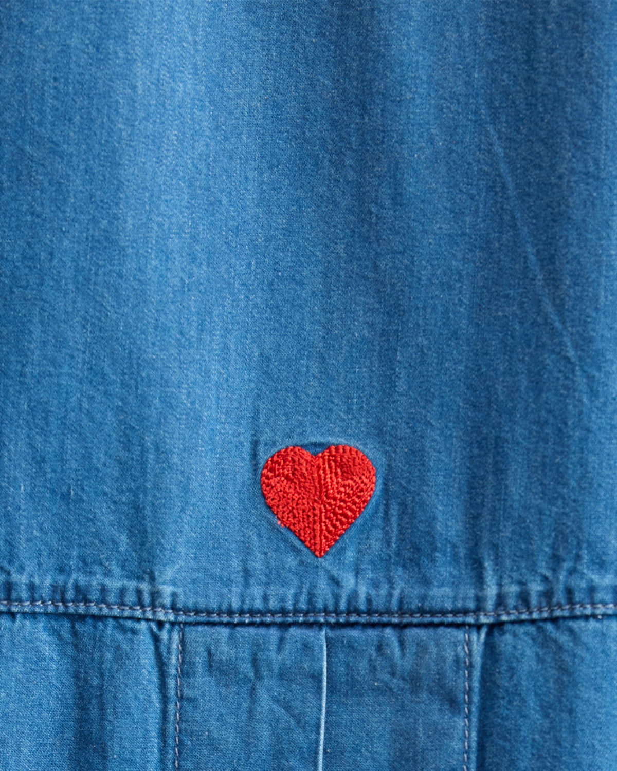 Close-up of a red heart embroidery on a blue denim Cirrus shirt.