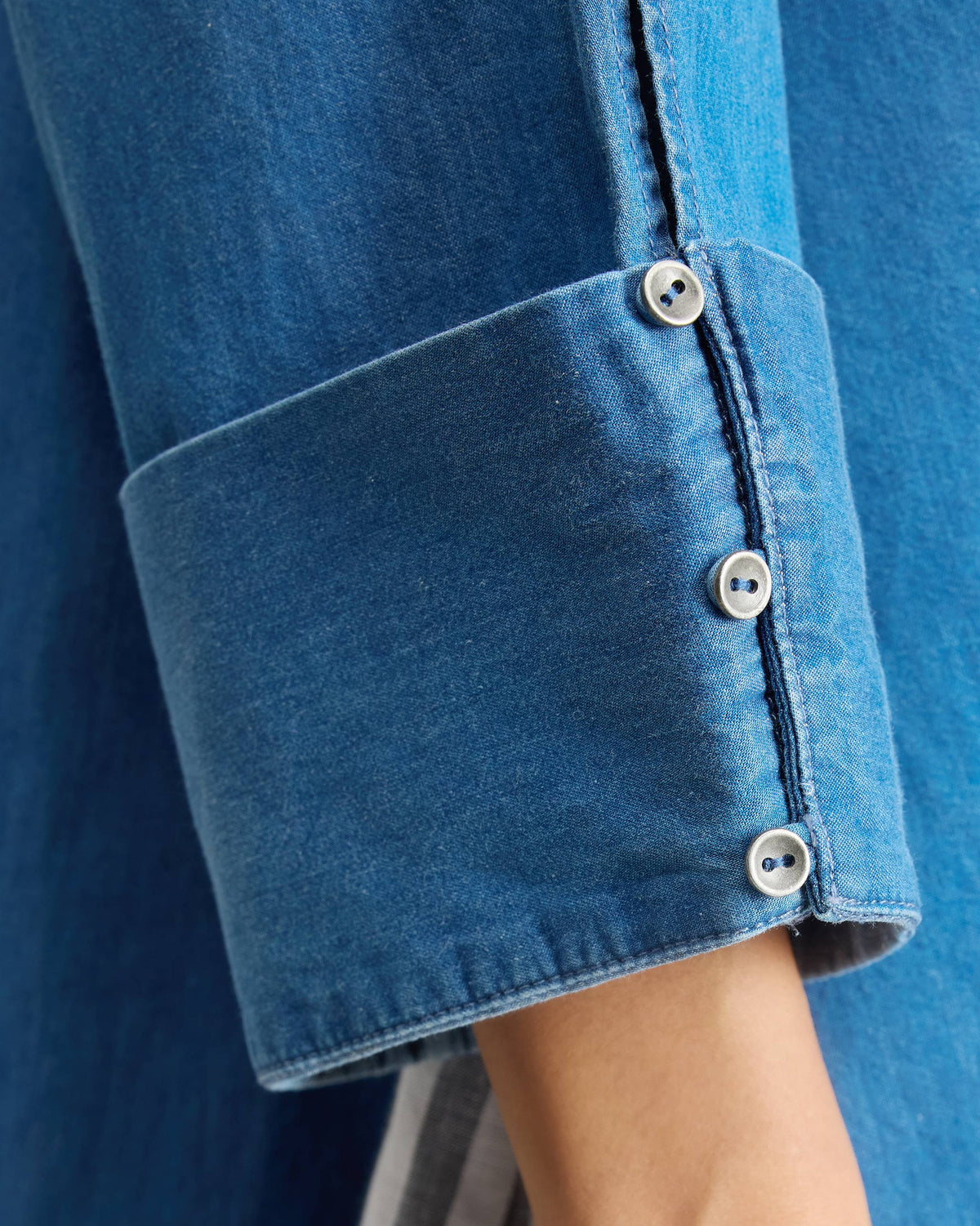 Close-up of silver cuff buttons on a blue denim Cirrus shirt.