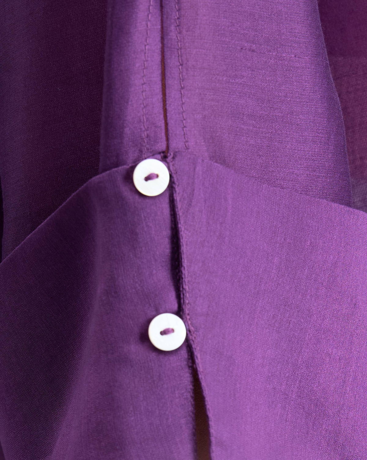 Close-up of white buttons on the purple Cirrus shirt fabric.