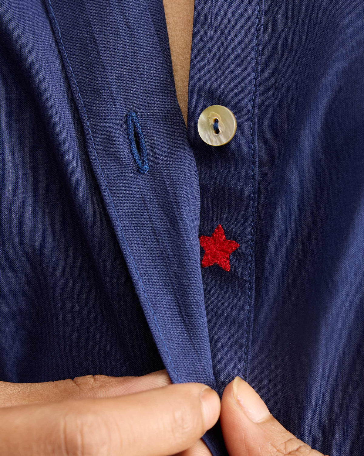 Close-up of a red embroidered star under the placket of an ink blue mid-length kurta.
