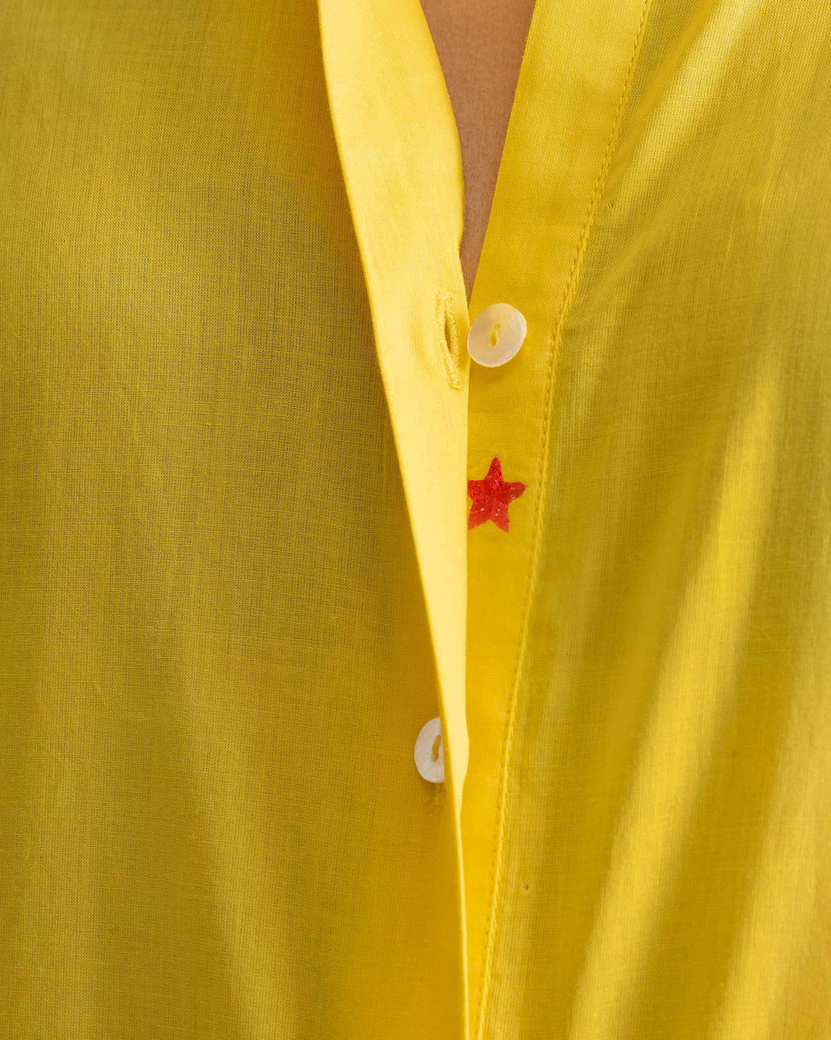 Close-up of a red embroidered star on the placket of a yellow kurta.