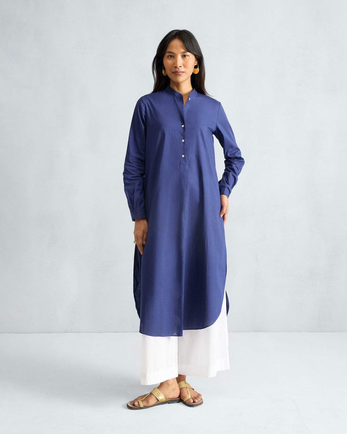 Person wearing an ink blue long kurta with buttoned cuffs and a curved hem.