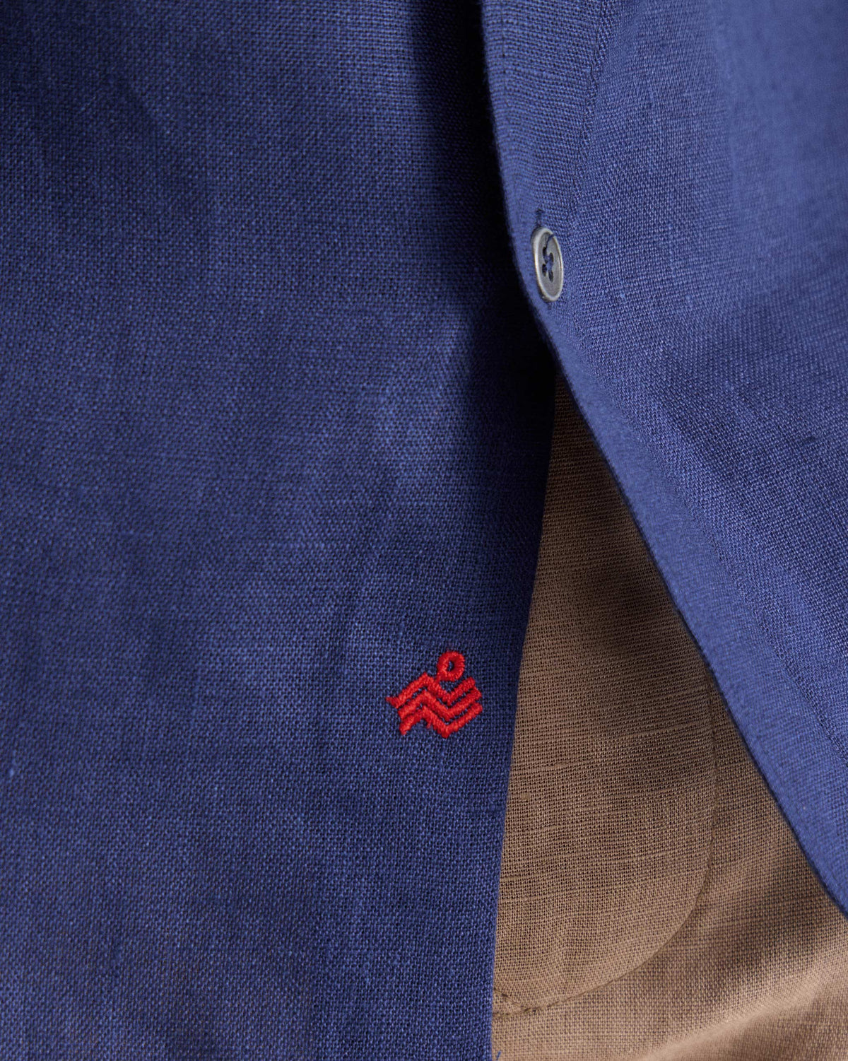 Close-up of red embroidery near the hem of an ink blue half-sleeve shirt.