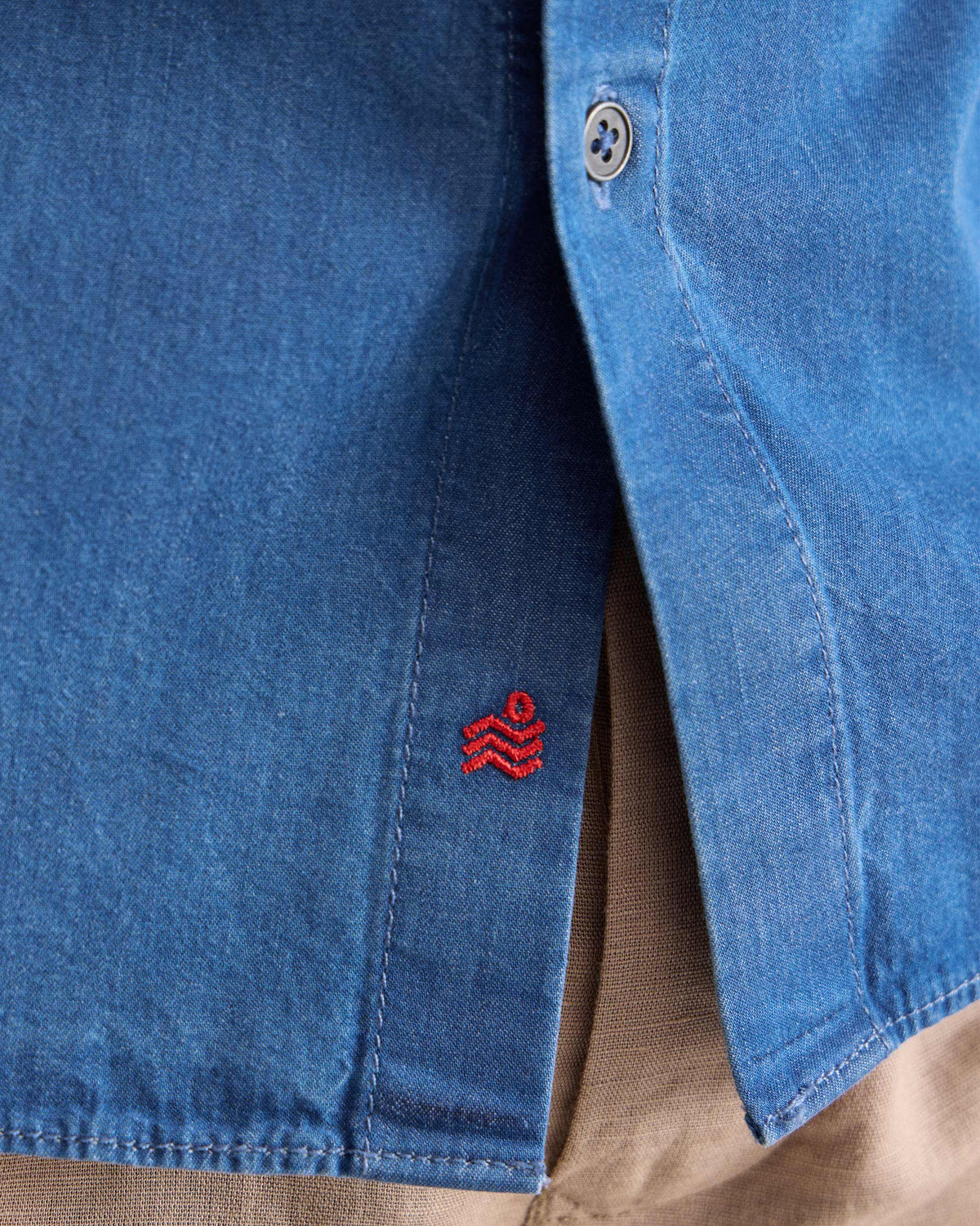 Close-up of red embroidery near the hem of a blue denim half-sleeve shirt.