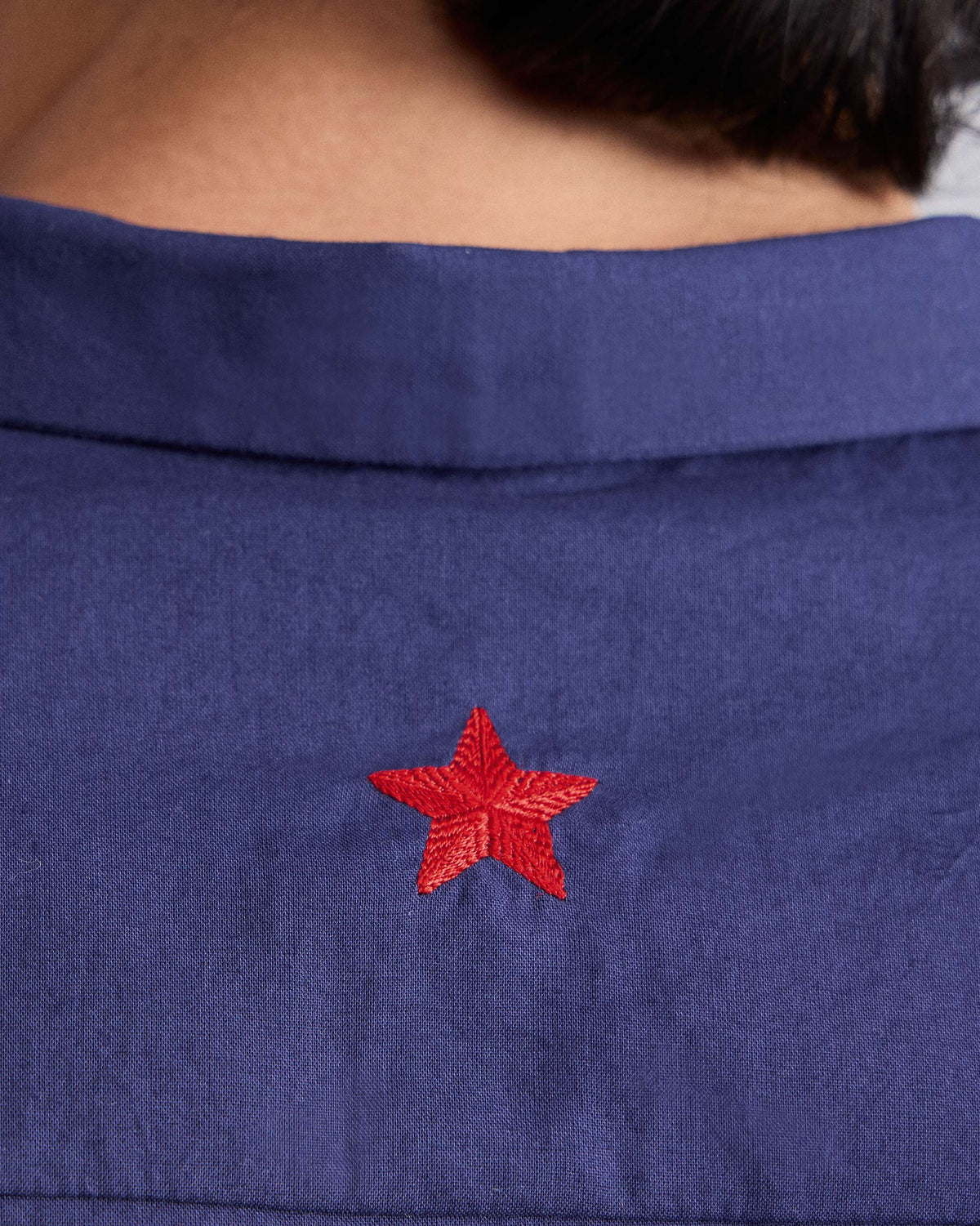 Close-up of a red star embroidered on the back of an ink blue Riverine Shirt.