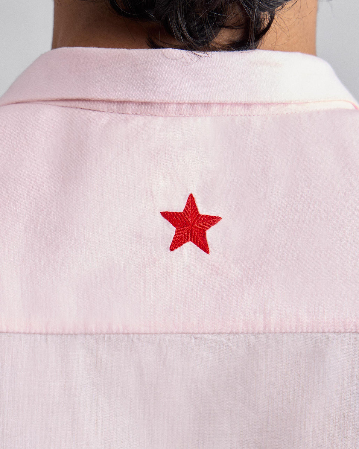 Close-up of a red star embroidered on the back of a pink Riverine Shirt.