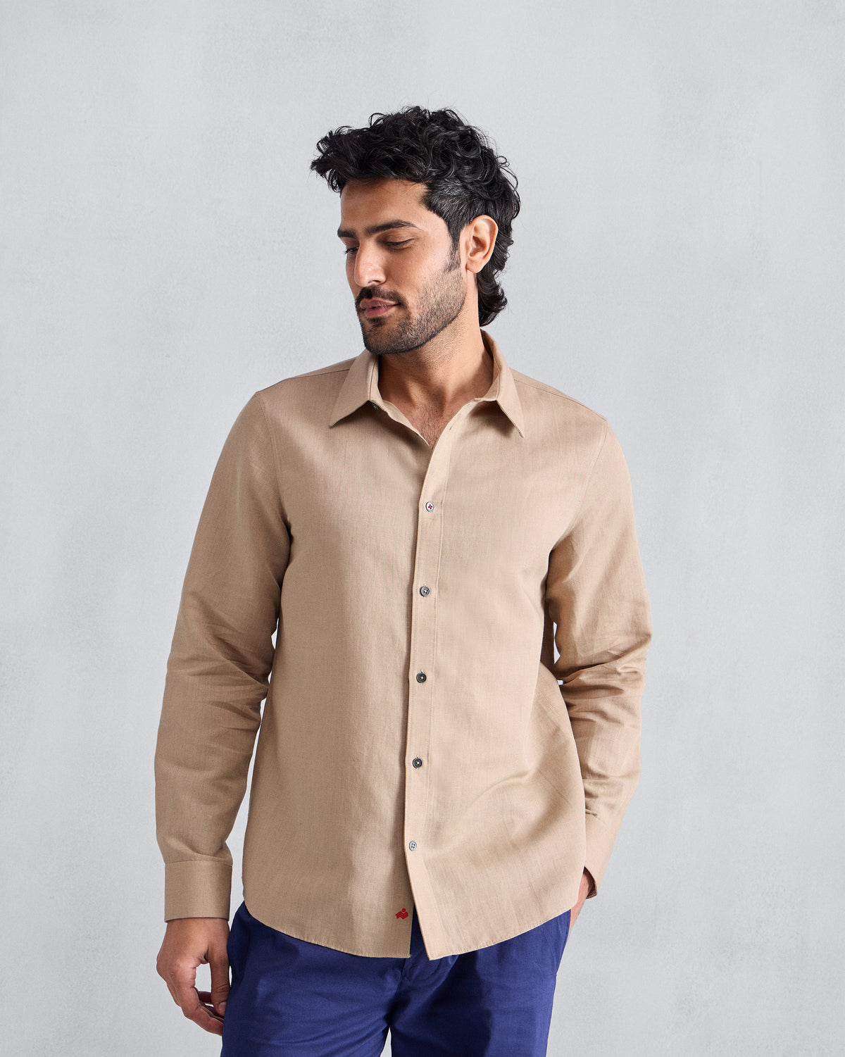 Person wearing a beige Classic shirt with a red hem logo.