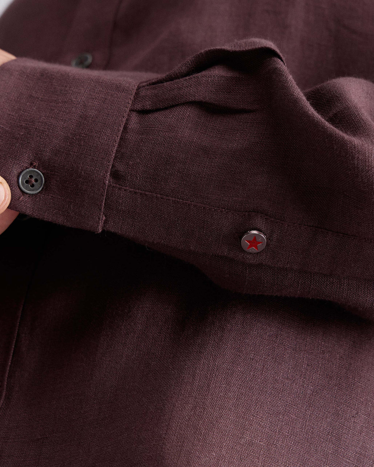 Close-up of a chocolate plum Classic shirt cuff with a red star button.
