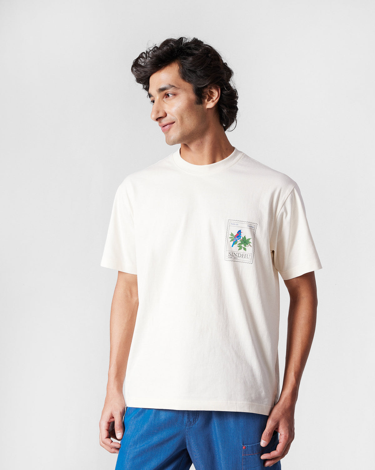 Person wearing an ivory Bulbul t-shirt with a bird stamp graphic.