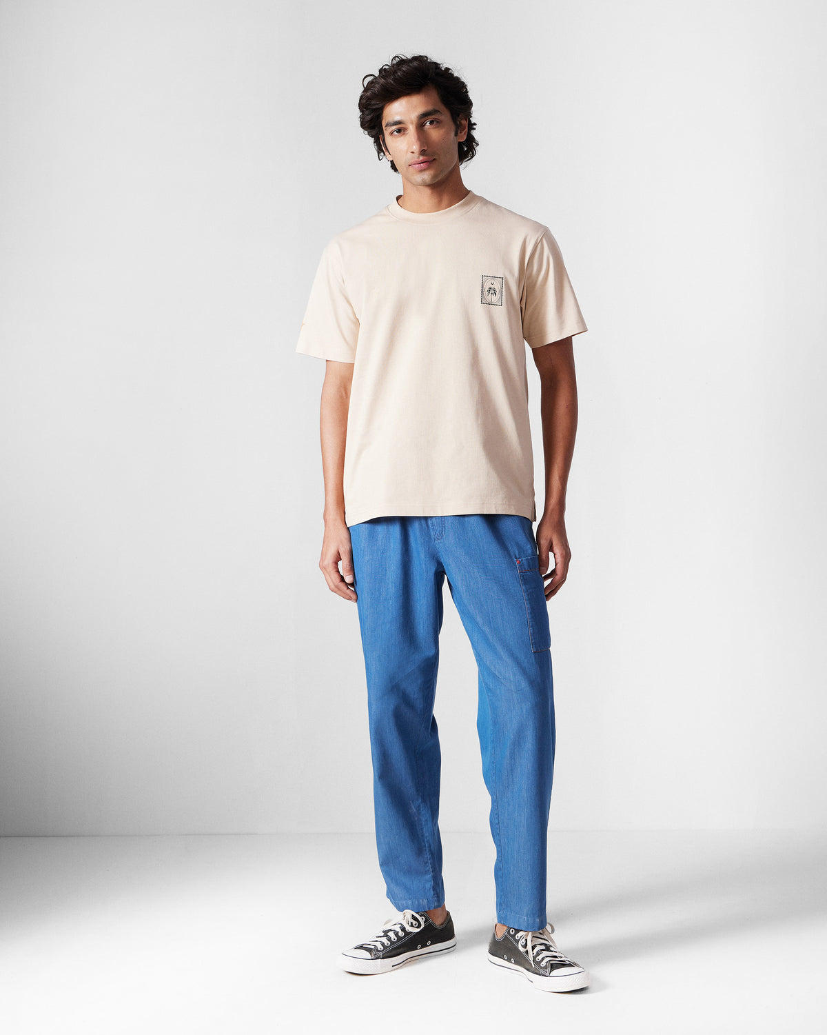 Person wearing a beige Postal T-Shirt with a small chest stamp.