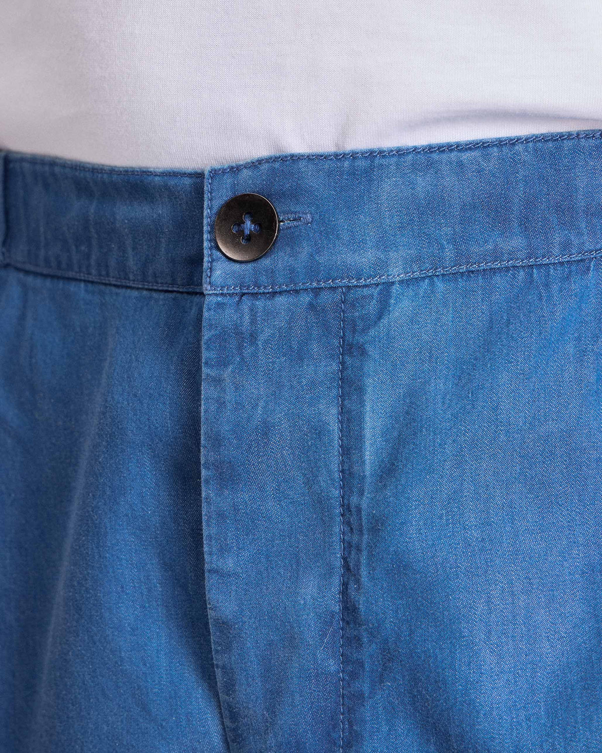 Close-up of denim blue Meadow Pants showing the button waistband and fly.