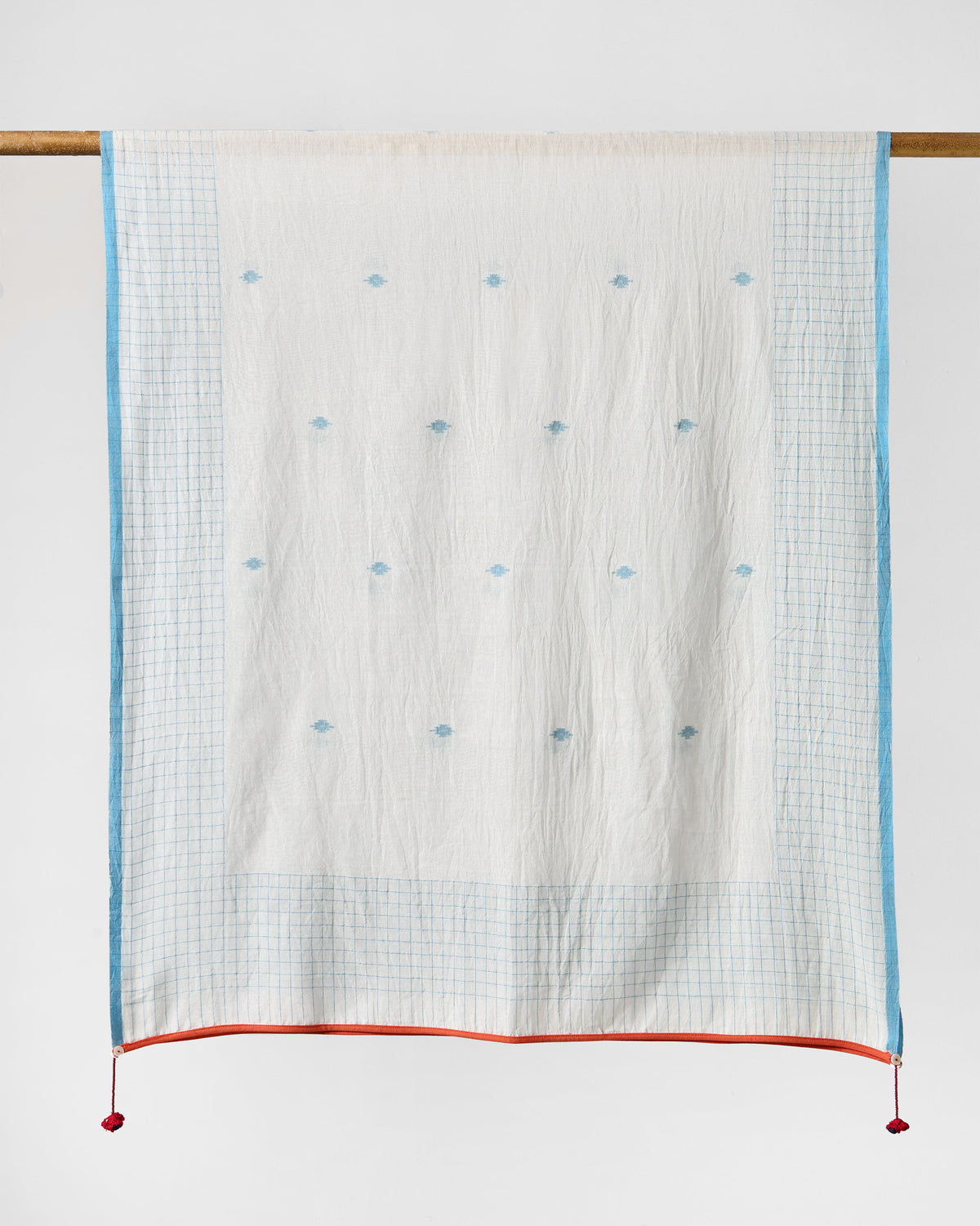 Full Checked Skies scarf hung from a rod, white with blue checks and small blue motifs.