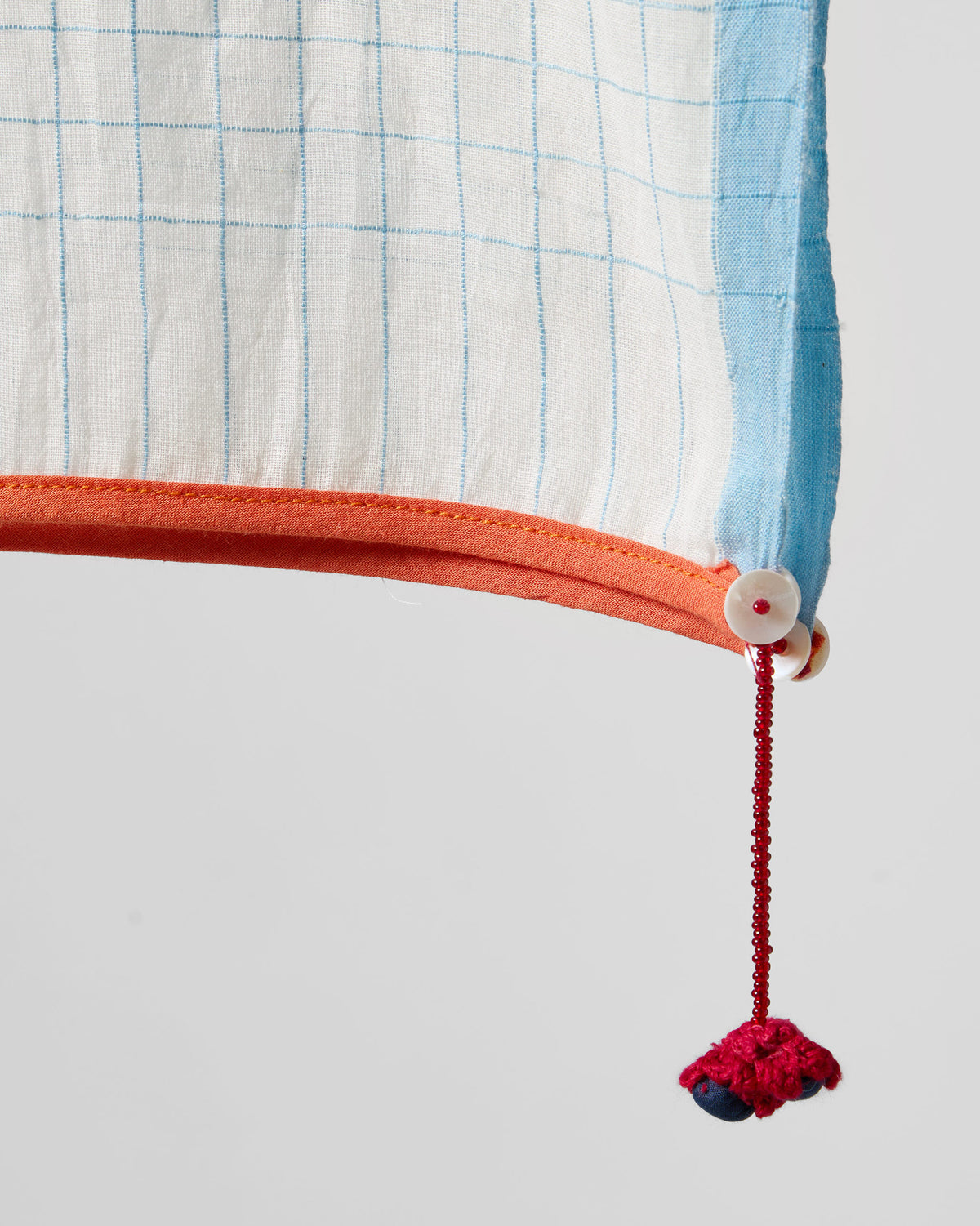 Close-up of the Checked Skies scarf corner showing blue checks, an orange edge and a red tassel.
