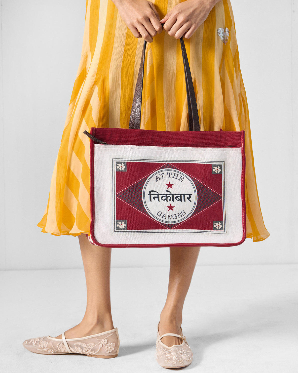 Ivory and red Ganges tote held by its brown leather straps.