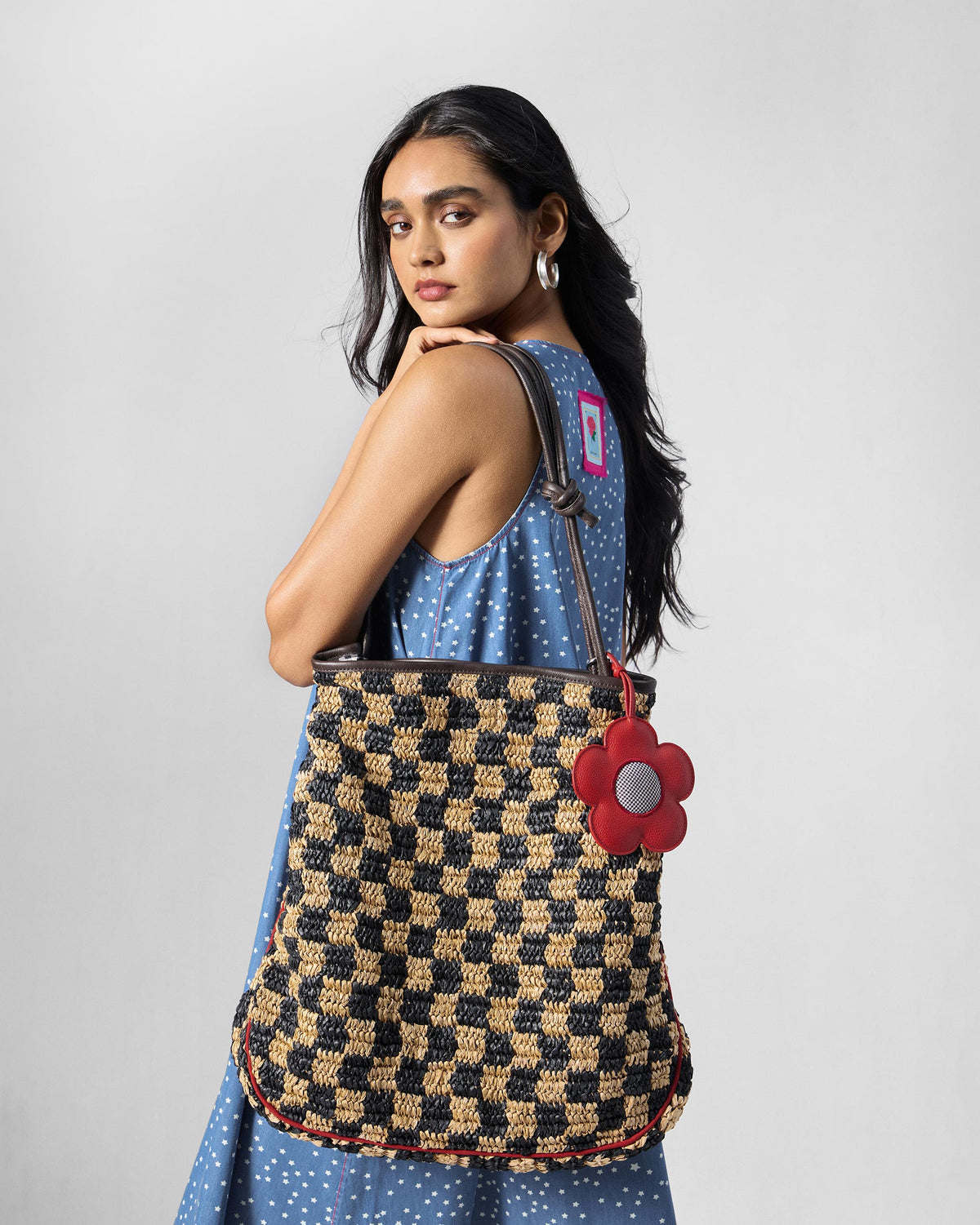 Person wearing a black and natural Nomad Tote with a red flower charm.