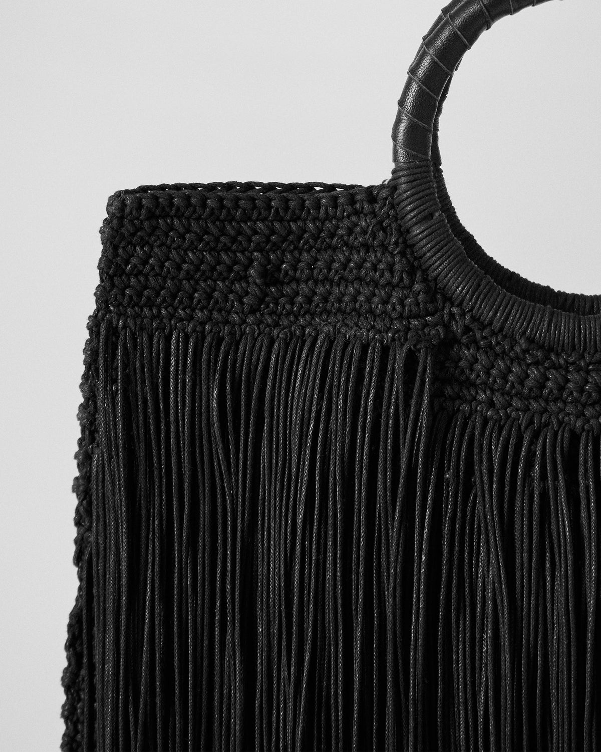Close-up of the circular handle on a black braided fringe bag.