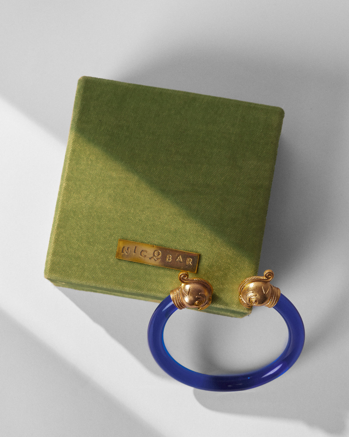 Blue Mithu Bangle with gold ends resting on a green gift box.
