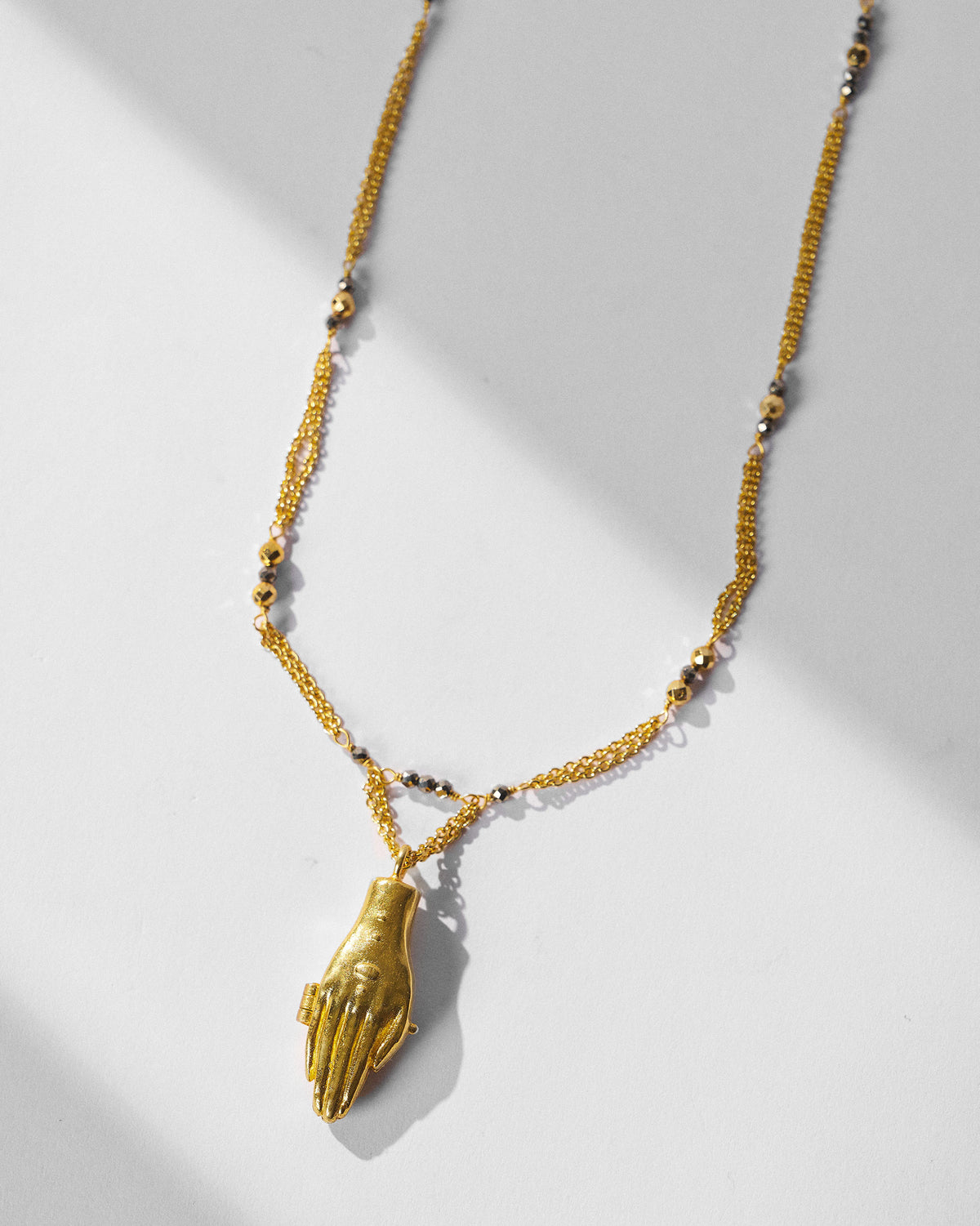 Gold Sama necklace with a sculpted hand pendant and dark beads.