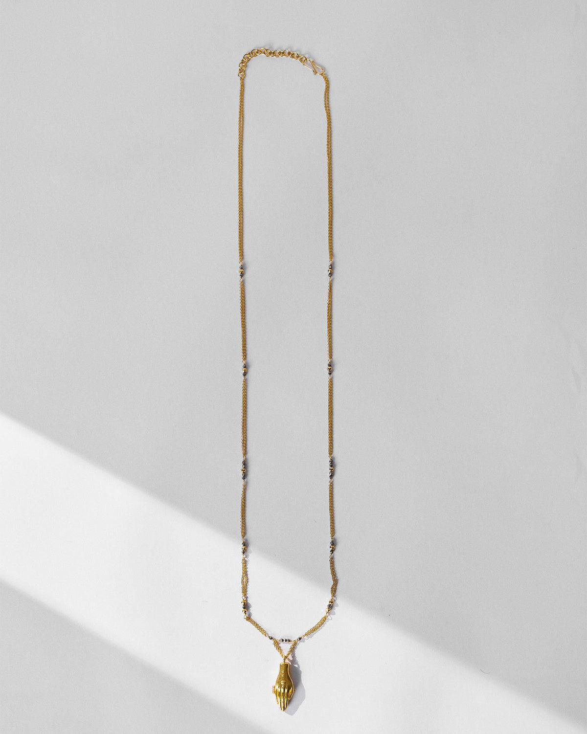 Long gold Sama necklace with a hand pendant and dark accent beads.