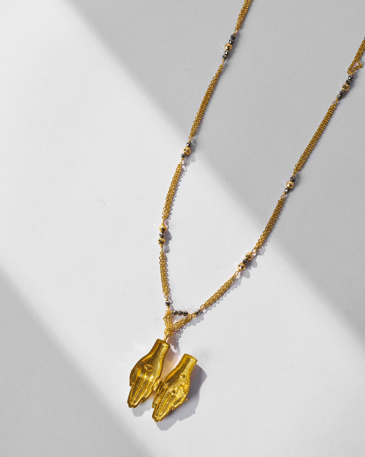 Gold Sama necklace with joined prayer-hands pendant and pyrite beads.