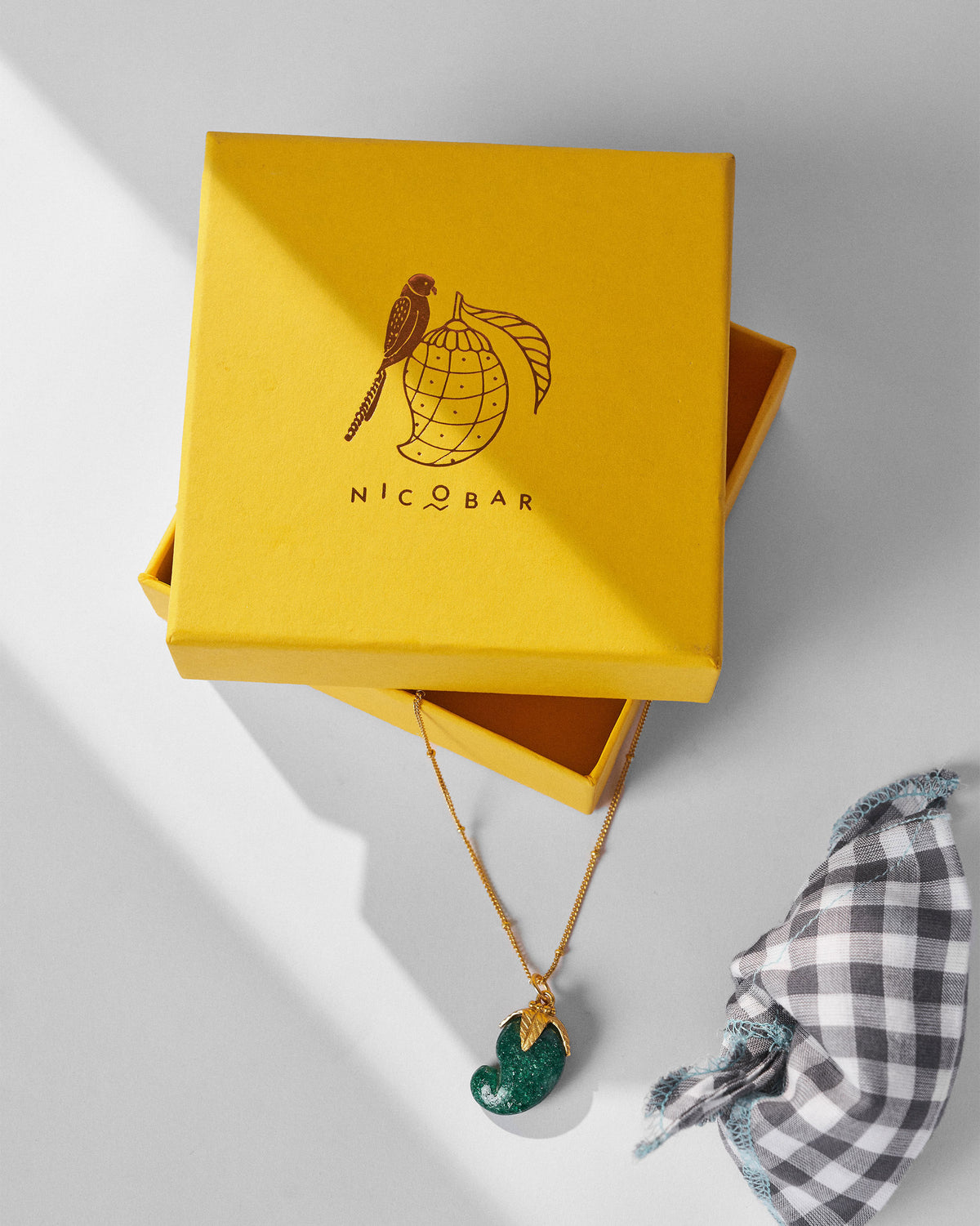 Gold Ambi necklace with a green pendant on a yellow Nicobar gift box.