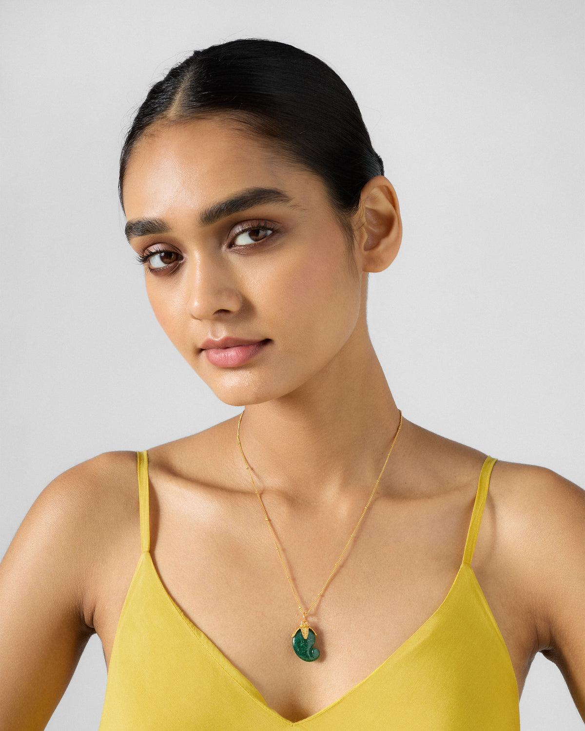 Person wearing a gold Ambi necklace with a green mango pendant.