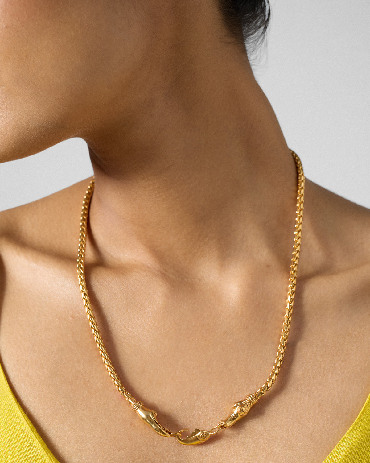 Person wearing a gold Makkar chain with makara heads and a fish clasp.