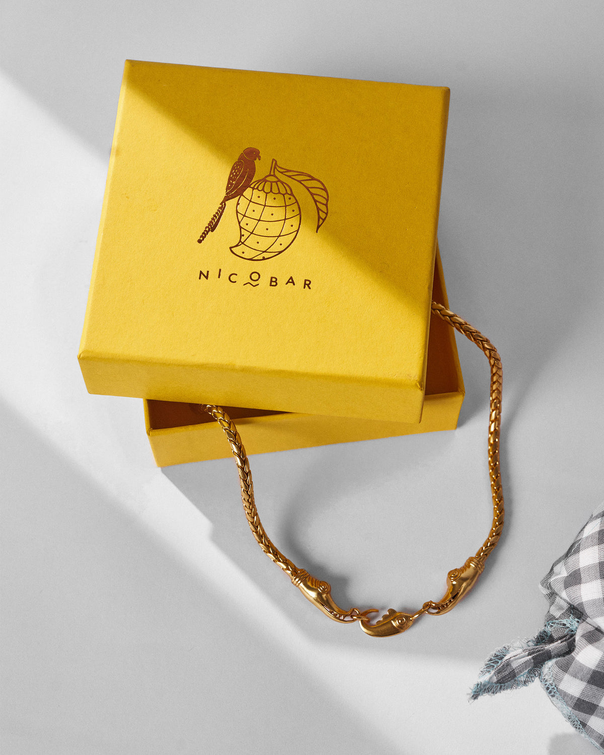 Gold Makkar chain with makara clasp draped from a yellow Nicobar gift box.