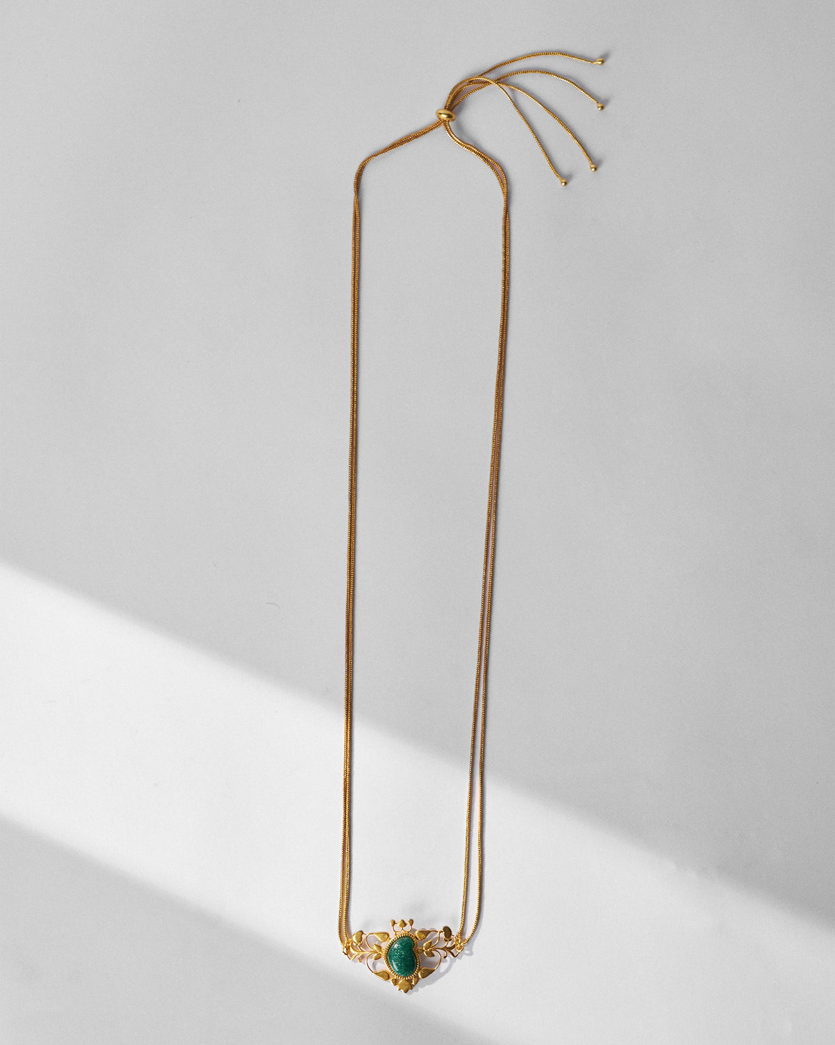 Gold Ambi choker laid flat with green stone pendant and adjustable clasp.