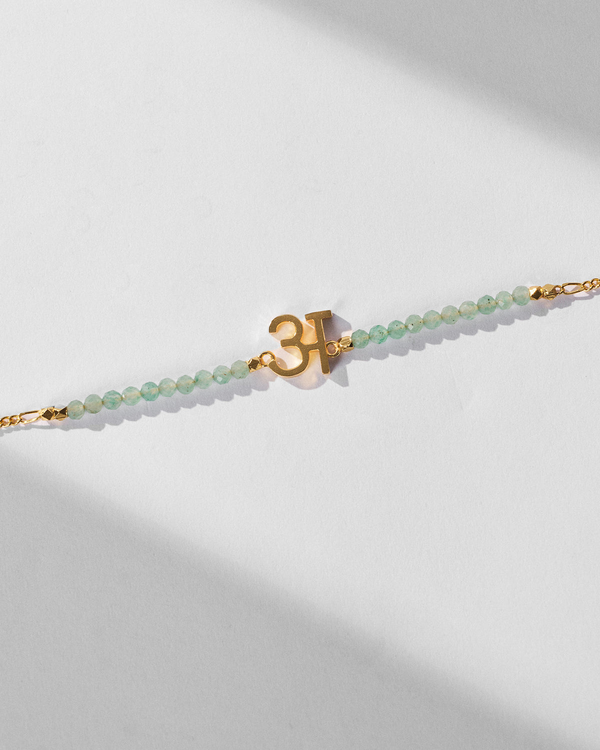 Angled view of Akshar Bracelet (A) - Gold with green beads and a gold charm.