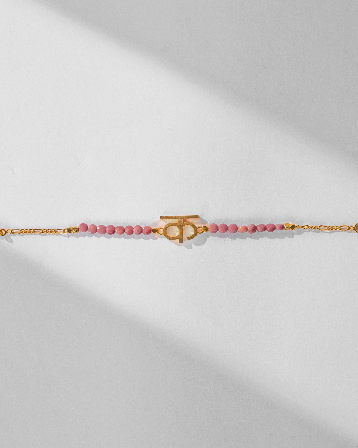 Gold Akshar K charm centered between dusty pink beads on a fine chain.