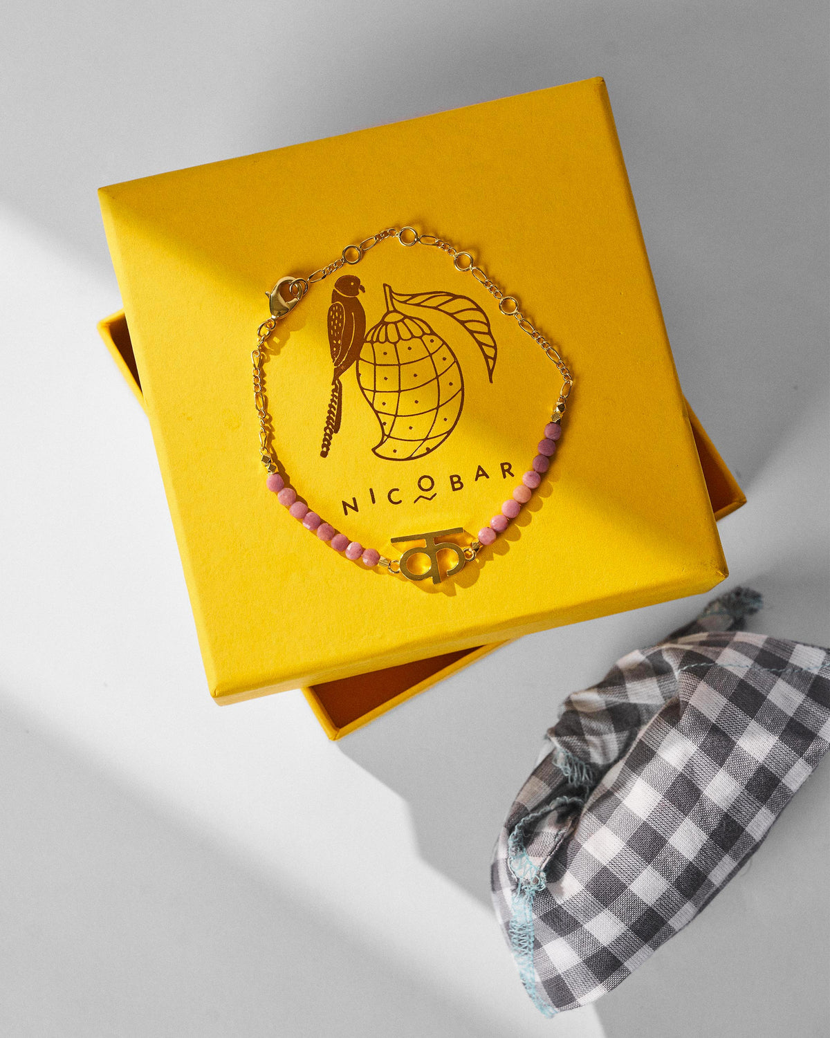 Gold Akshar K bracelet draped on a yellow Nicobar gift box.