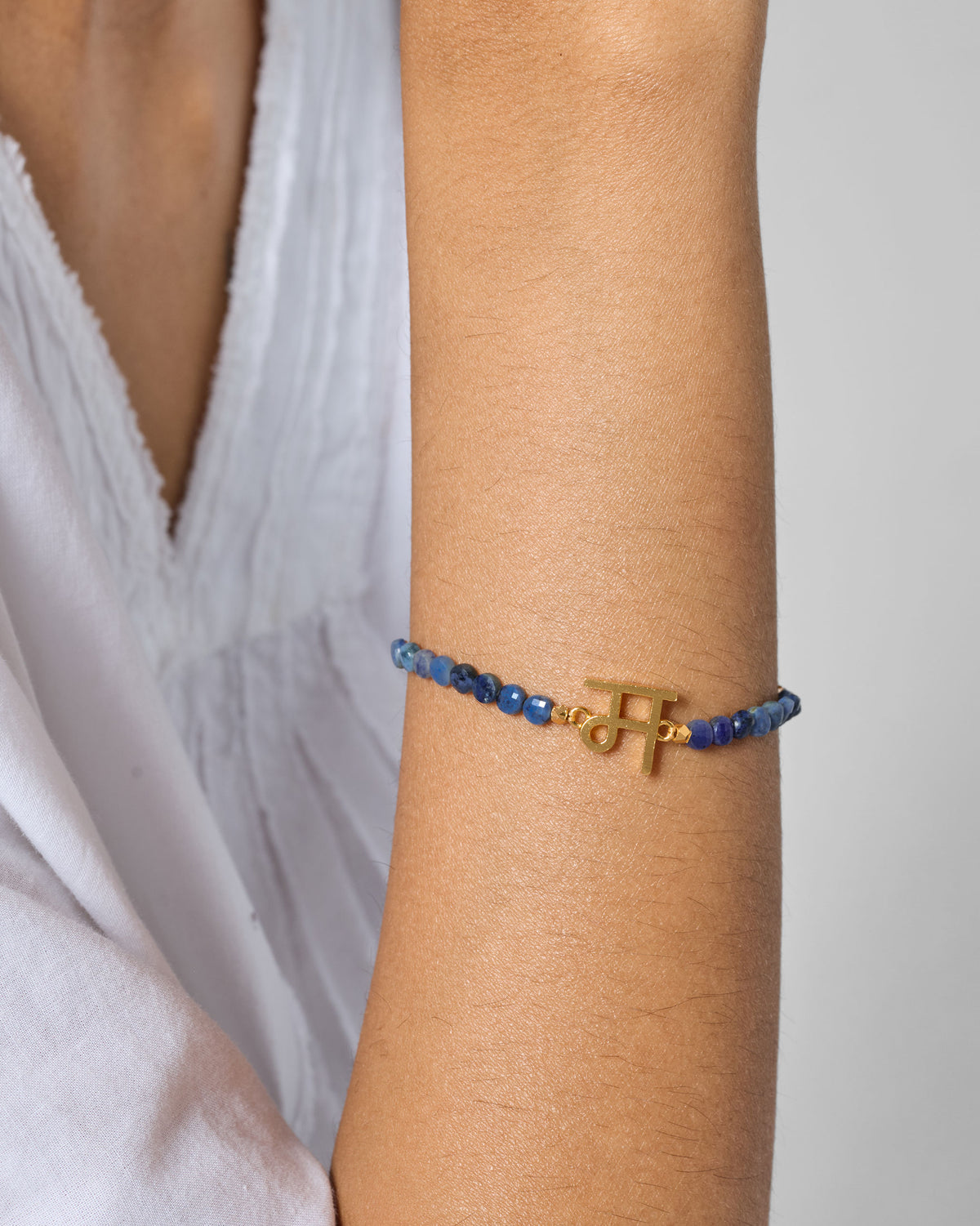 Person wearing Akshar Bracelet (M) - Gold with blue beads on the forearm.